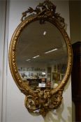An oval gilt wall mirror moulded with scrolls and candle mount. Est. £20 - £30.
