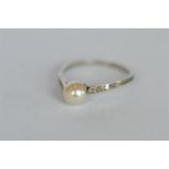 A pearl single stone ring set with diamond shoulders. Est. £220 - £250.