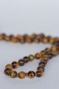 A string of tiger's eye beads with small concealed clasp. Est. £10 - £15.