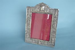 A large Eastern silver frame, heavily decorated with figures. Approx. 29 cms high. Est. £70 - £80.