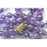 A graduated string of amethyst beads with gold clasp. Est. £30 - £50.