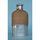 A silver hip flask with hinged cover and wicker bo