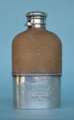 A silver hip flask with hinged cover and wicker bo