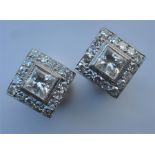 A pair of 18 carat white gold ear studs, the central princess cut stones surrounded by a border of