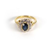 A yellow metal ring set a single oval sapphire in a surround of ten diamonds, ring size O