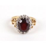 An 18ct yellow gold ring set oval ruby in a surround of twelve diamonds in a fleur de lis mount,