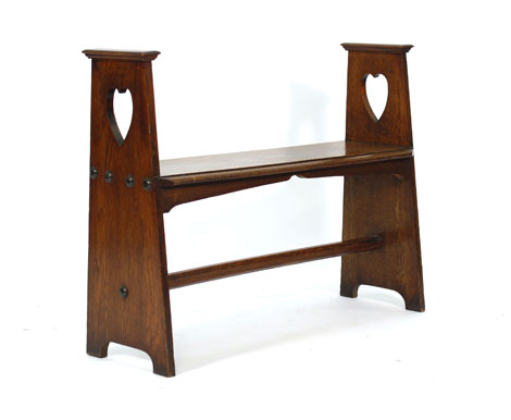 An Arts & Crafts oak bench, the two supports with heart shaped decoration and joined by a stretcher,