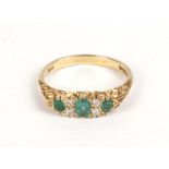 An 18ct yellow gold ring set three graduated emeralds interspersed with four small diamonds,