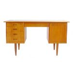 A 1970's teak desk with an arrangement of five drawers and one door on circular tapering legs, l.