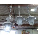 A set of three grey enamelled ceiling lights on shafts with steel grills and moulded glass shades