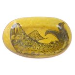 A 1960/70's studio pottery dish decorated with a stylised fish on a yellow ground, l. 41 cm