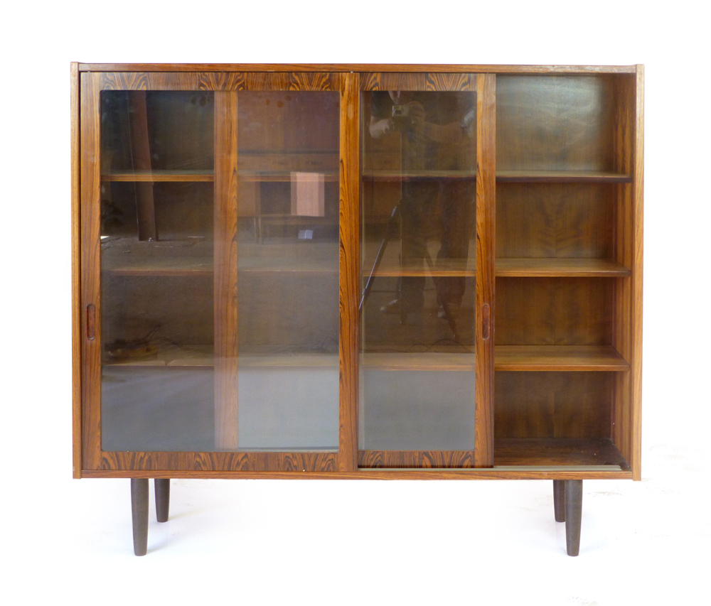 A 1960's rosewood bookcase with twin glazed sliding doors and six adjustable shelves on circular