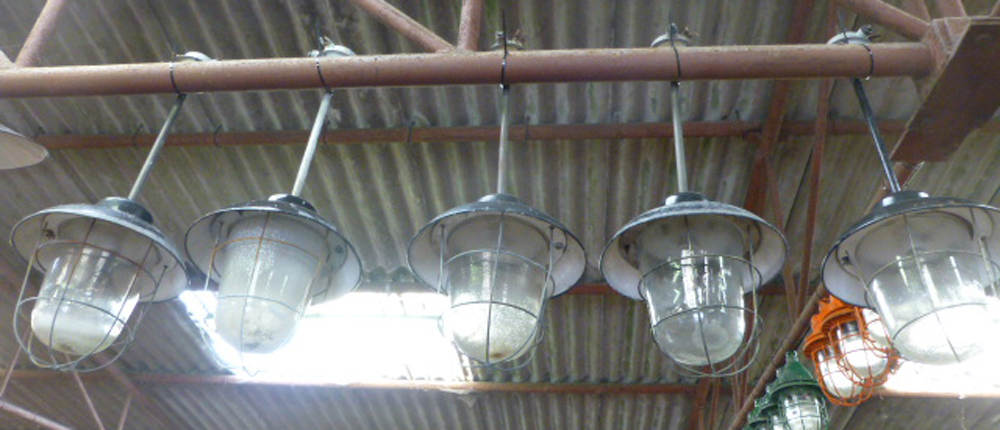 A set of five black enamelled ceiling lights on metal shafts with steel grills and moulded glass