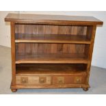 A contemporary bookcase with three shelves above two drawers with brass handles and raised on bun