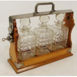 An oak and metal mounted tantalus with three clear cut glass decanters, with key, width 35cm.