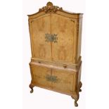 A 20th century walnut Epstein style cocktail cabinet with shell carved pediment and twin door