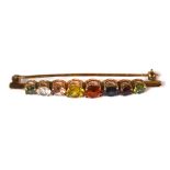 An Edwardian yellow metal bar brooch set with various coloured stones to include green, amber,