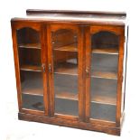 A 20th century free standing glazed three door oak bookcase with interior shelving on plinth base,