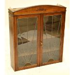 A mid 20th century oak hanging display cupboard with curved pediment above a pair of hinged doors