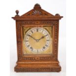 An Edwardian oak cased eight day mantel clock with shaped top above single glazed door with carved