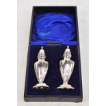A cased pair of Edward VII hallmarked silver urn shaped peppers with fluted corners raised on oval