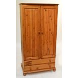 A pine wardrobe with pair of doors enclosing a shelf and a rail rack above two long drawers and