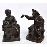 A pair of 19th century bronze figures, both seated, the man wearing a hat and sitting on his coat,