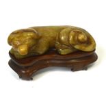 A Chinese carved russet included jade model of a lying dog on shaped rosewood stand, length 7.5cm.