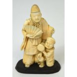 A Japanese Meiji period carved ivory okimono of a standing figure holding a fan beside a kneeling