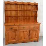 A modern pine dresser, boarded plate rack above three drawers and lower cupboard sections,