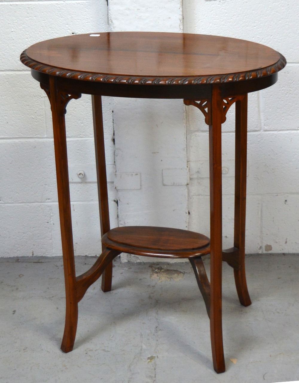 An Edwardian oval walnut side table with lower shelf supported by carved fretwork on splayed