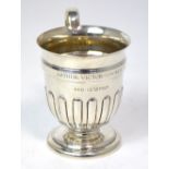 A George V hallmarked silver christening cup with high loop handle and gadrooned body to spreading