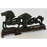 A large modern carved green hardstone group of two running horses on a shaped wooden plinth,
