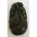 A Chinese dark green jade carving of a mythical beast climbing two incised decorated fruits with