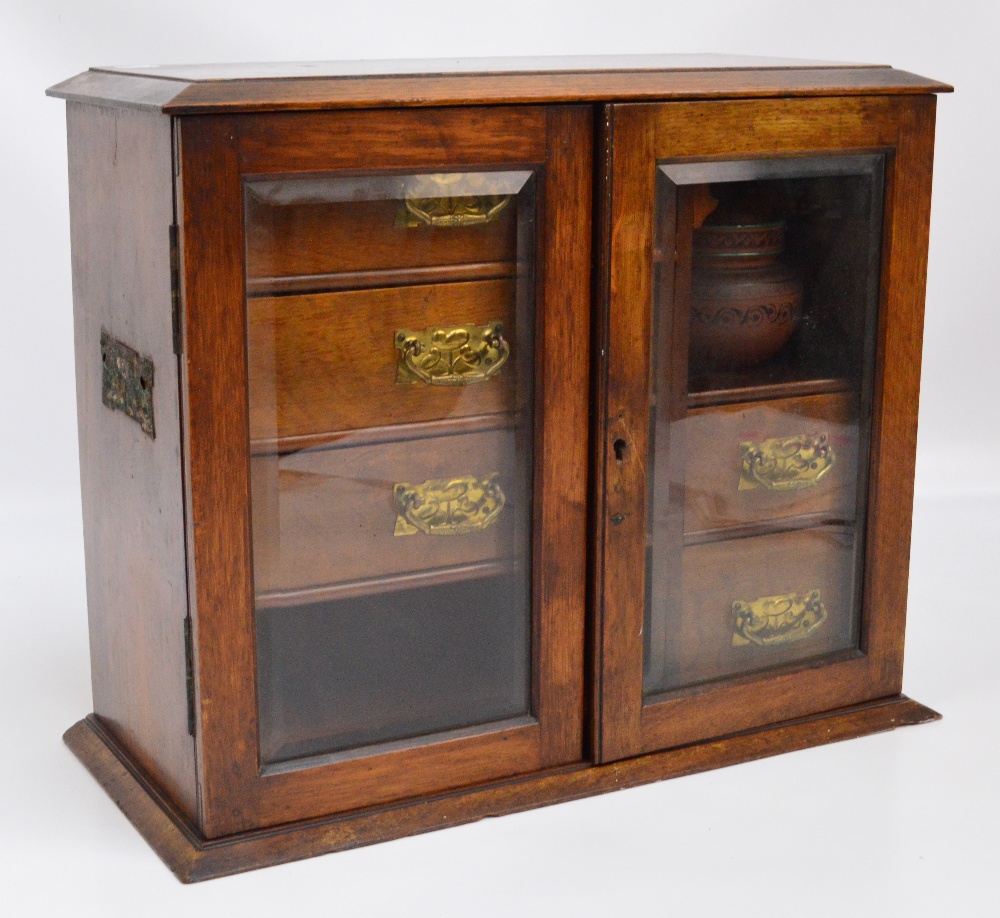 An Edwardian oak smoker's cabinet with a pair of glazed doors enclosing a formation of three