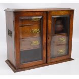 An Edwardian oak smoker's cabinet with a pair of glazed doors enclosing a formation of three