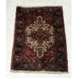 A red rug with central beige medallion within geometrical motifs and decorative border, 91 x 140cm.