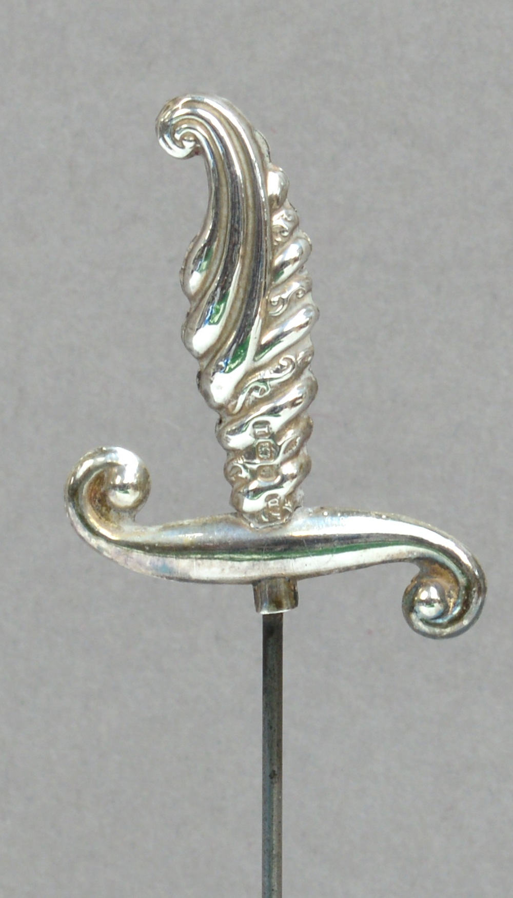 A George V hallmarked silver hat pin in the form of a sword hilt with swathed and curved guard,