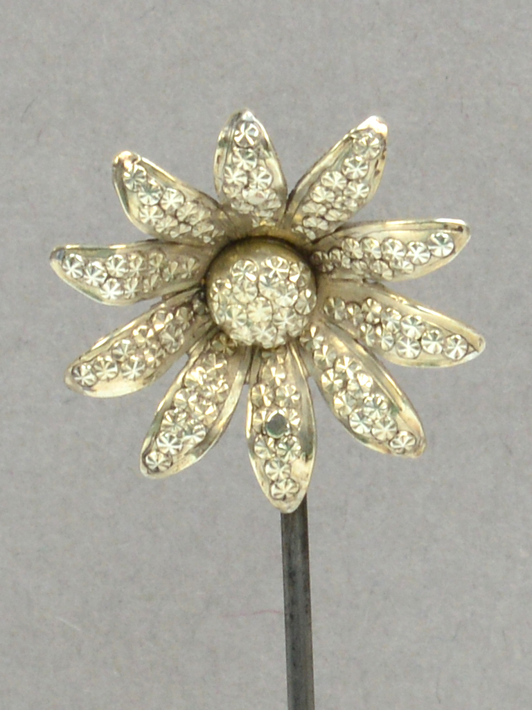 A white metal hat pin in the form of a daisy head with star punched decoration to the petals and