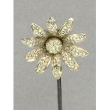 A white metal hat pin in the form of a daisy head with star punched decoration to the petals and