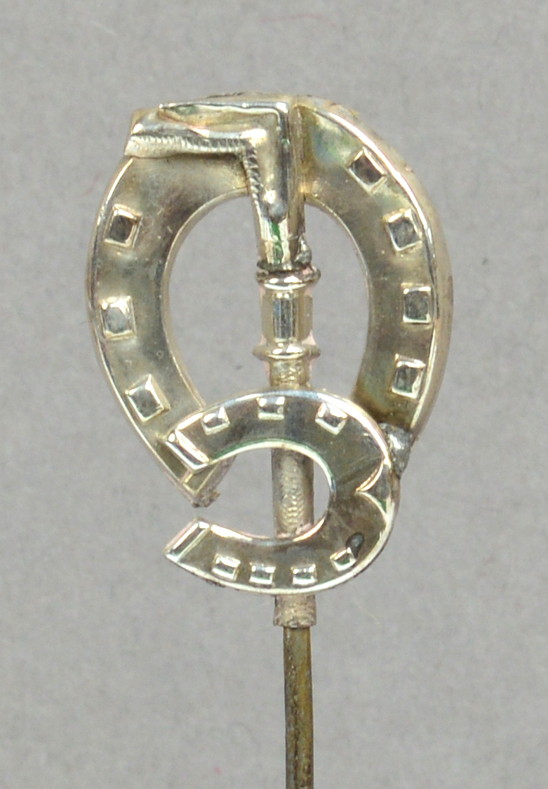 A George V hallmarked silver hat pin in the form of a riding crop with mare and colt horseshoes,