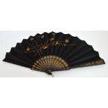 A Victorian folding fan with ebonised wooden guards and sticks with gilt motifs,