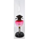 An oil lamp with painted pink font on rounded stepped ebonised base, height 61cm.