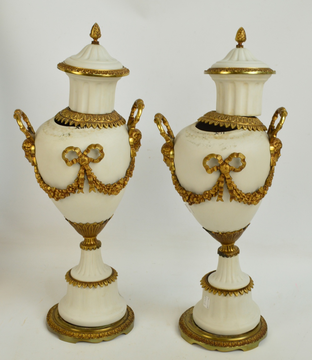 A pair of decorative porcelain and gilt metal mounted urns with twin mask handles between opposing