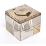 A George V hallmarked silver mounted clear glass inkwell of plain square form, with hinged lid,