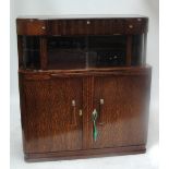 An Art Deco oak cocktail cabinet, with three hinged compartments above sliding glass doors,