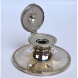 An Edwardian hallmarked silver capstone type inkwell with hinged circular lid enclosing a glass