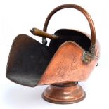 A helmet shaped copper coal scuttle with swing handle raised on a circular foot, width 50cm,