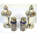 A pair of loaded sterling silver shakers and a smaller pair of silver plated blue glass lined pots