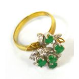 A 14ct white gold dress ring set with emeralds and diamonds in a scrolling floral design setting,